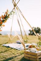 Boxes with festive treats stand near the wedding tipi arch on a green lawn photo