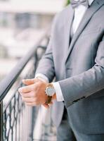 Groom in a suit fastens his watch strap while standing on the balcony. Cropped. Faceless photo