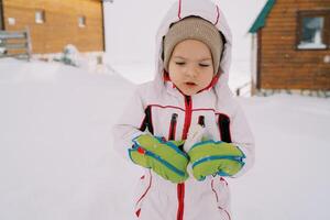 Little girl stands in the snow near wooden houses and looks down photo