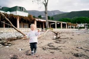 Little girl with a pebble in her hand walks along the beach against the backdrop of the house photo