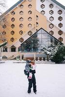 madre con un pequeño niña en su brazos soportes en frente de un triangular hotel en el nieve foto