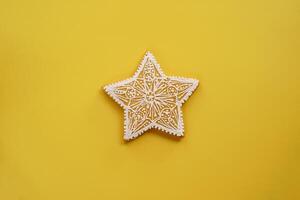 Glazed openwork white gingerbread star lies on a yellow background photo
