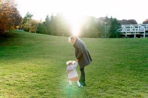 Little girl pulls her mom by the hand along the green lawn. Back view photo