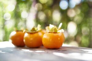 Ripe persimmons lie in a row on a wooden table on a balcony in the sun photo