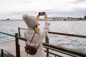 Traveler takes pictures of the coast of a resort town with moored yachts with a smartphone. Back view photo