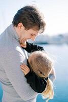 Smiling dad holds a little girl hugging his shoulder while standing by the sea photo