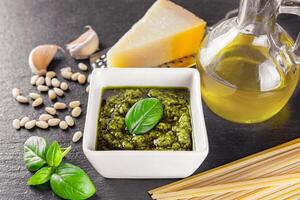 Homemade pesto sauce in small square jar and ingredients for pasta on black stone background photo