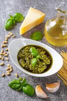 Homemade pesto sauce in small glass jar and ingredients for pasta on gray concrete background photo