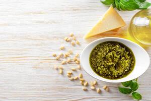 Homemade pesto sauce in small jar and ingredients for pasta on white wooden background photo