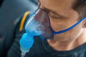 Close up view of unhealthy man wearing nebulizer mask in home. Health, medical equipment and people concept. High quality photo