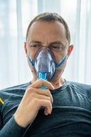 Unhealthy man wearing nebulizer mask in home. Health, medical equipment and people concept. High quality photo