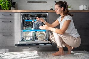 A woman removes clean ceramic dishes from dishwasher. Household and useful technology concept. High quality photo