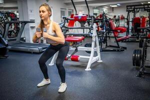 joven mujer sostiene pesas en su manos y trabajos fuera en el gimnasio ejecutando un ejercicio. alto calidad foto