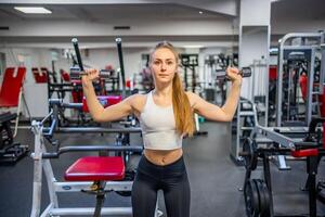 Young woman holds dumbbells in her hands and works out in the gym performing an exercise. High quality photo