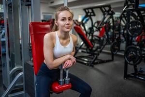 joven mujer posando con pesas en su manos y trabajos fuera en el gimnasio ejecutando un ejercicio. alto calidad foto