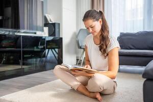 Young woman reads book sitting on the floor in the living room photo