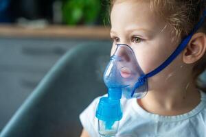 cerca arriba ver de pequeño niña son sentado y participación un nebulizador máscara propensión en contra el rostro, vías respiratorias tratamiento concepto. alto calidad foto