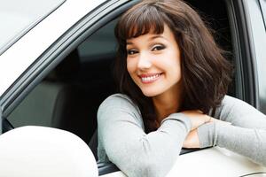 bonito mujer conductor sonriente a usted desde el blanco coche foto