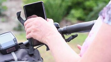 Jeune femme installe une téléphone intelligent sur le guidon de une vélo dans une spécial monter pour la navigation, pour vivre diffusion sur social les réseaux, choisir une cyclisme itinéraire,haut qualité 4k métrage video