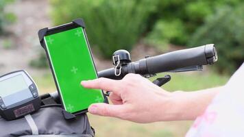 young woman using smartphone with green screen mockup mounted on bike handlebar to navigate maps app, selecting bike route, High quality 4k footage video