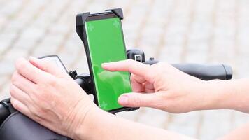 young woman using smartphone with green screen mockup mounted on bike handlebar to navigate maps app, selecting bike route, High quality 4k footage video