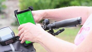 young woman using smartphone with green screen mockup mounted on bike handlebar to navigate maps app, selecting bike route, High quality 4k footage video