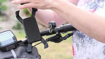 joven mujer instala un teléfono inteligente en el bigote daliniano de un bicicleta en un especial montar para navegación, para En Vivo radiodifusión en social redes, elegir un ciclismo ruta, alta calidad 4k imágenes video