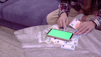 jovem mulher conta euro notas usando uma Smartphone calculadora com uma verde tela, em a sofá dentro uma quarto às casa, o menina calcula a orçamento, poupança, ganhos, alta qualidade tiroteio dentro 4k formato video