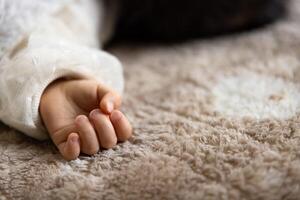 un izquierda mano de dormido asiático bebé en el alfombra foto