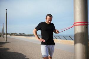 atlético hombre hacer ejercicio con elástico resistencia aptitud banda al aire libre foto