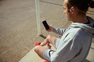 Overhead view sportsman wearing earphones, using smartphone with blank black mockup digital touch screen after workout photo