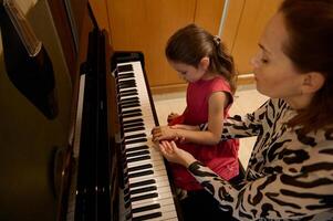 pequeño niño niña teniendo un piano lección con su maestro. hembra pianista explicando el correcto posición de manos en piano llaves. musical educación y talento desarrollo en progreso. parte superior ver foto
