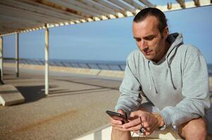Young man browsing fitness app on mobile phone, scrolling newsfeed, checking social media content in Atlantic promenade photo