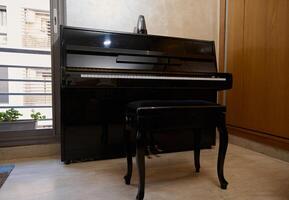 Interior of a room with stylish black piano and backless stool against large window background photo