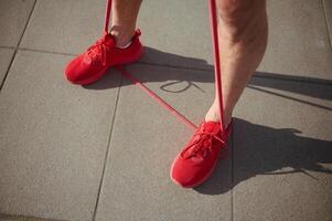 ver desde encima de atlético hombre en rojo Deportes zapatos, haciendo físico ejercicios con rojo resistencia banda foto