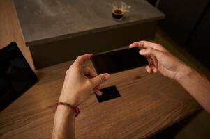 Hand holding mockup smartphone screen, scanning black empty credit card for making online payments via internet banking photo