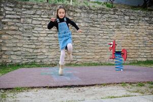 un pequeño niño niña saltando en uno pierna, jugando rayuela en un urbano patio de recreo al aire libre. rayuela popular calle juego foto