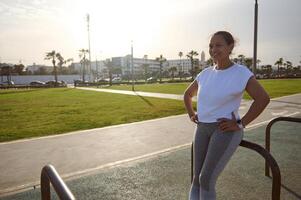 Portrait of a smiling happy young sportswoman on the sportsground after morning workout outdoors photo