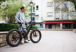 joven hombre en Deportes tener puesto, alquiler y montando bicicletas eléctricas en el ciudad. bicicleta compartiendo ciudad Servicio foto