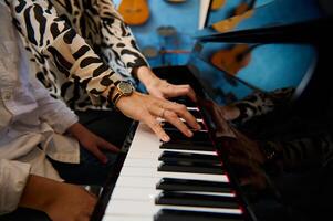 de cerca mujer profesor manos conmovedor piano llaves mientras jugando grandioso piano con su estudiante chico en el música clase foto