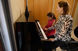 confidente auténtico hembra pianista, música profesor dando un individual piano lección a su pequeño alumno. musical educación y talento desarrollo en Progreso foto