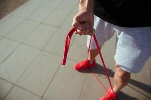 Top view of sportsman in red sneakers, gray sports shorts and black t-shirt doing warm up exercises with resistance band photo