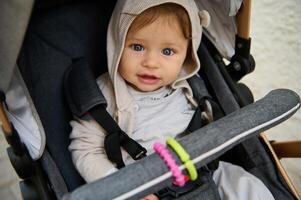 Authentic portrait of a Caucasian cute baby boy sitting in baby pram outdoors, smiling cutely looking at camera photo