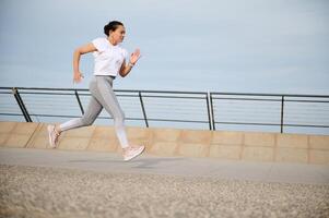 Active sporty woman athlete enjoys a morning workout, jogging, running on the city bridge. Healthy lifestyle concept photo