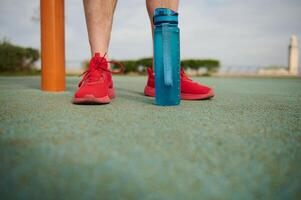 recortado ver de Atletas pies en rojo zapatillas y botella de agua en el campo deportivo. Copiar anuncio espacio foto