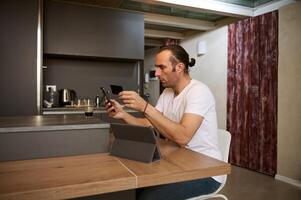 Man making online payments via internet mobile banking, sitting at table with smart phone and credit card in his hands photo