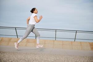 Side portrait of a woman running on the city bridge, performing her morning jog, exercising outdoors photo