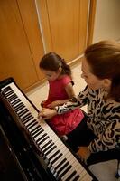 Overhead view of a female pianist musician holding the hands of a little child girl, showing the true position of finger on piano keys, explaining the piano lesson during individual music class photo