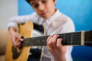 detalles en el manos de Adolescente chico guitarrista músico punteo instrumentos de cuerda mientras jugando el acústico guitarra durante un música lección. aficiones y ocio foto