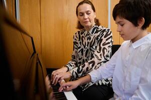 adolescente colegial jugando piano con su profesor durante individual música lección a hogar. musical educación y artístico desarrollo para joven personas y niños foto